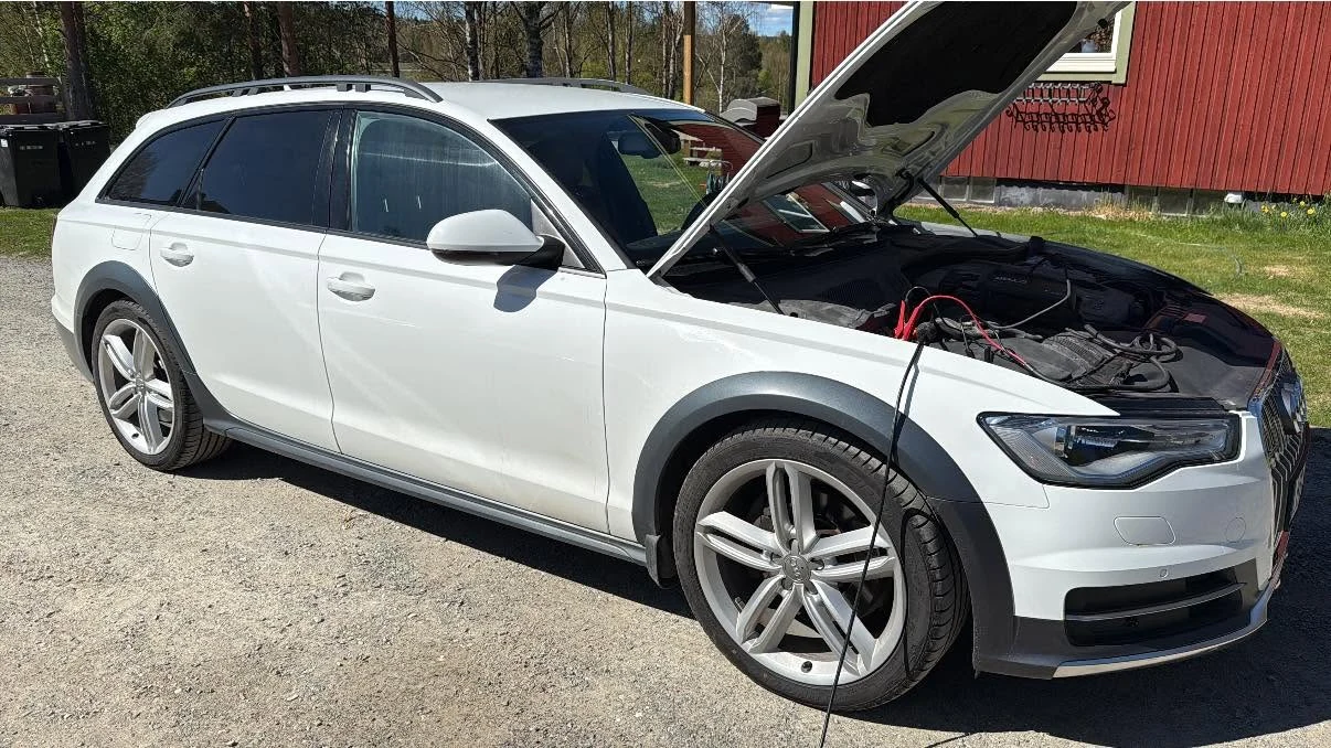 Audi Allroad med öppen motorhuv på gården framför röd lada